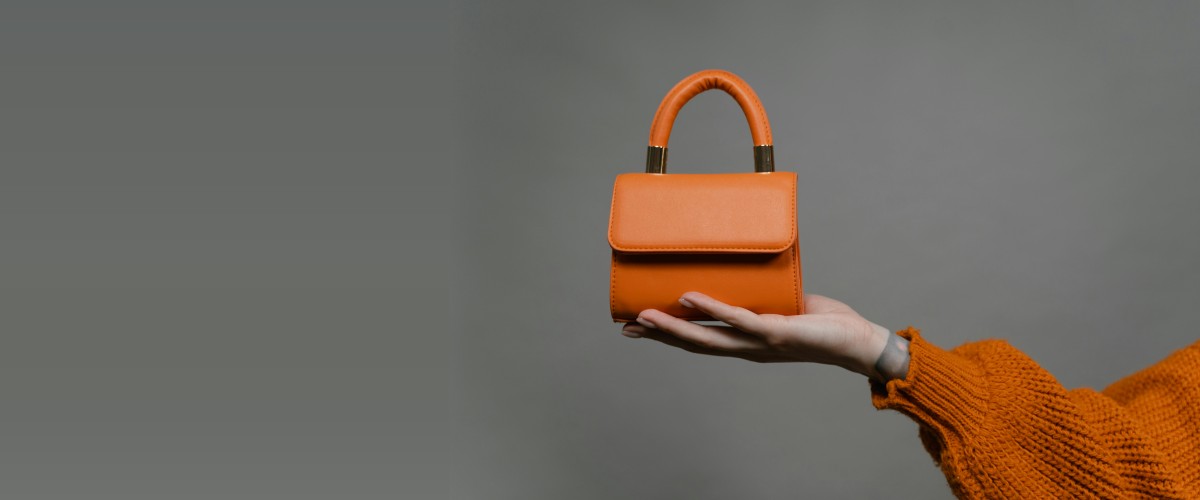 Orange handbag held in a hand against a gray background