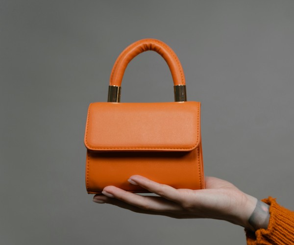 Orange handbag held in a hand against a gray background