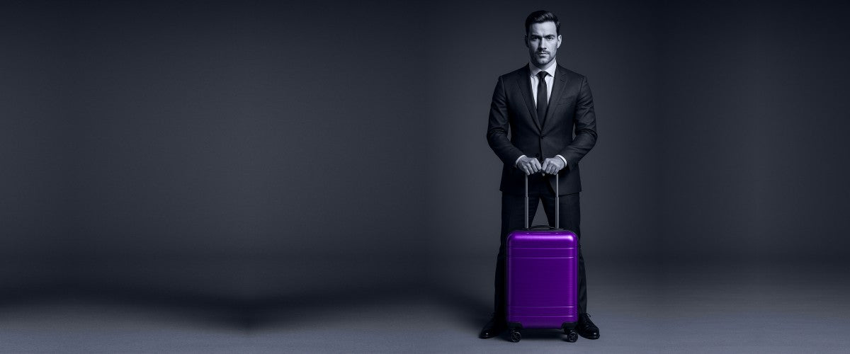 Man in a suit standing next to a purple suitcase on a dark background
